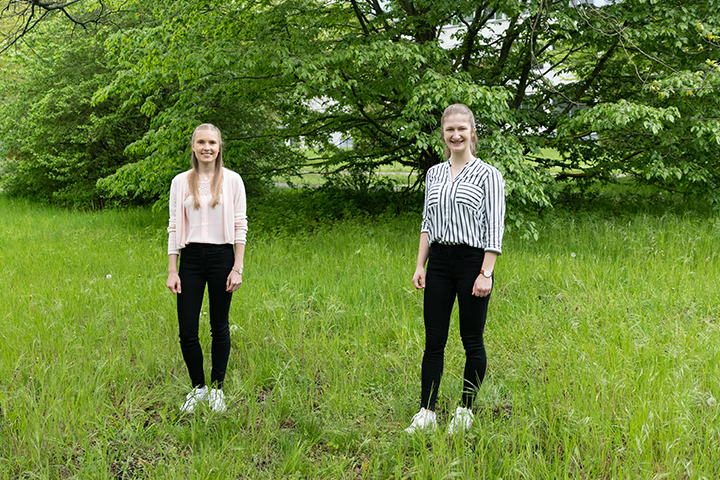 Emily Narten und Anja Tiede stehen mit Abstand auf einem Stück Rasen mit grünen Büschen im Hintergrund.