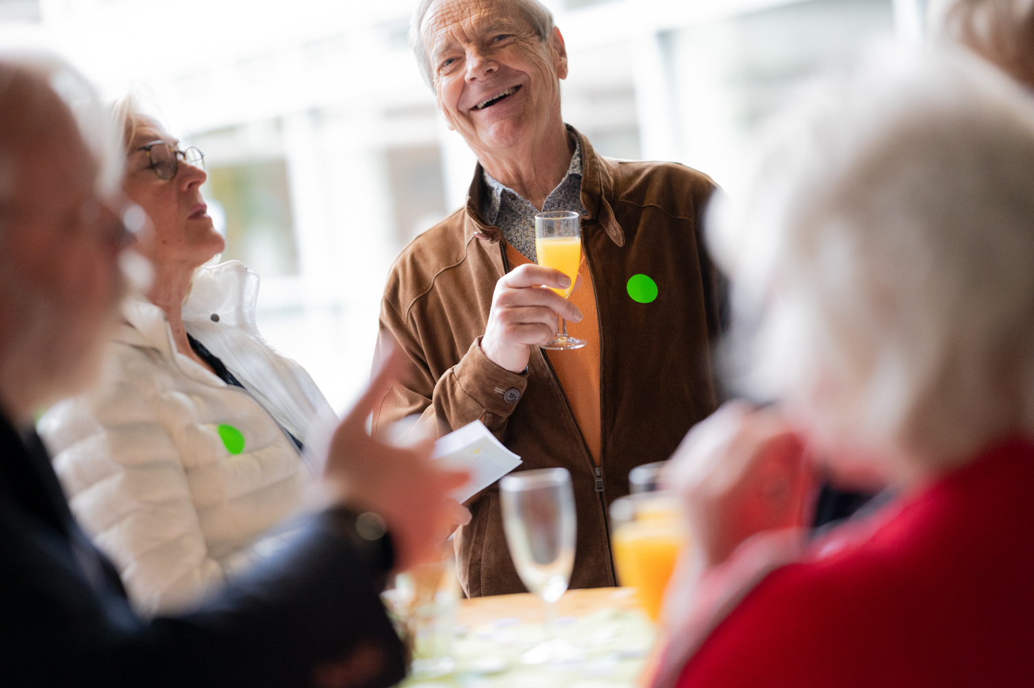 Ein Mann mit einem O-Saft-Glas in der Hand lacht.