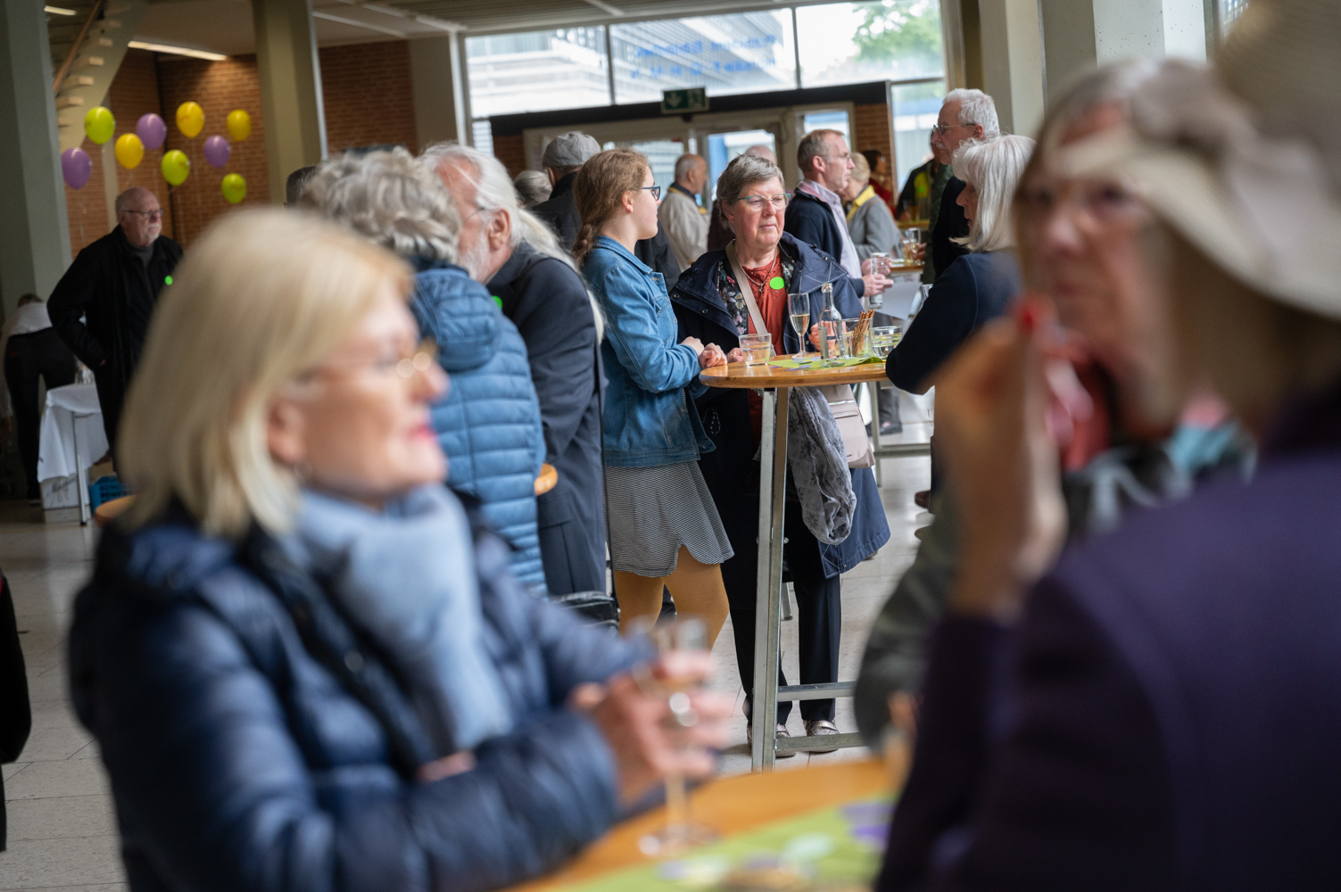 Menschen stehen an Stehtischen oder anderswo in Grüppchen und unterhalten sich. 