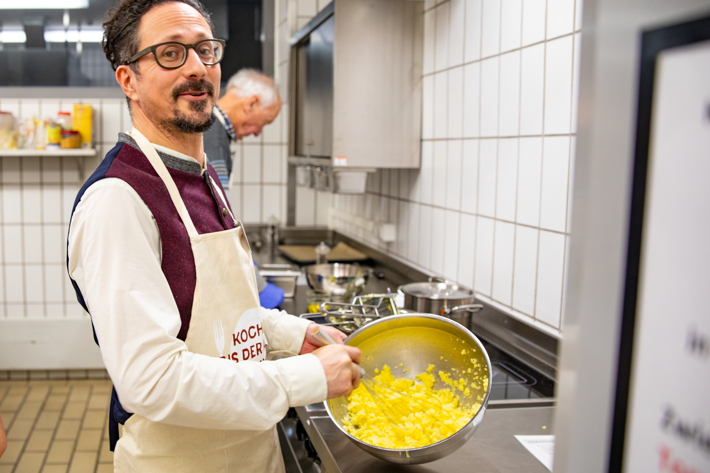 Mann mit Brille rührt eine gelbe Masse an und lächelt in die Kamera.