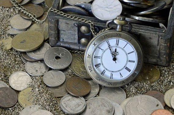 Eine Taschenuhr ist an eine kleine Truhe gelehnt. In und vor der Truhe liegen verschiedene Münzen verstreut.