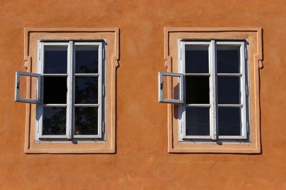 Eine braune, verputzte Hauswand mit zwei Sprossenfenstern, die nebeneinander liegen. Die Streben in den Fenstern teilen die Scheiben in je sechs kleine Quadrate auf. In beiden Fenstern ist das mittelere, linke Quadrat geöffnet. 