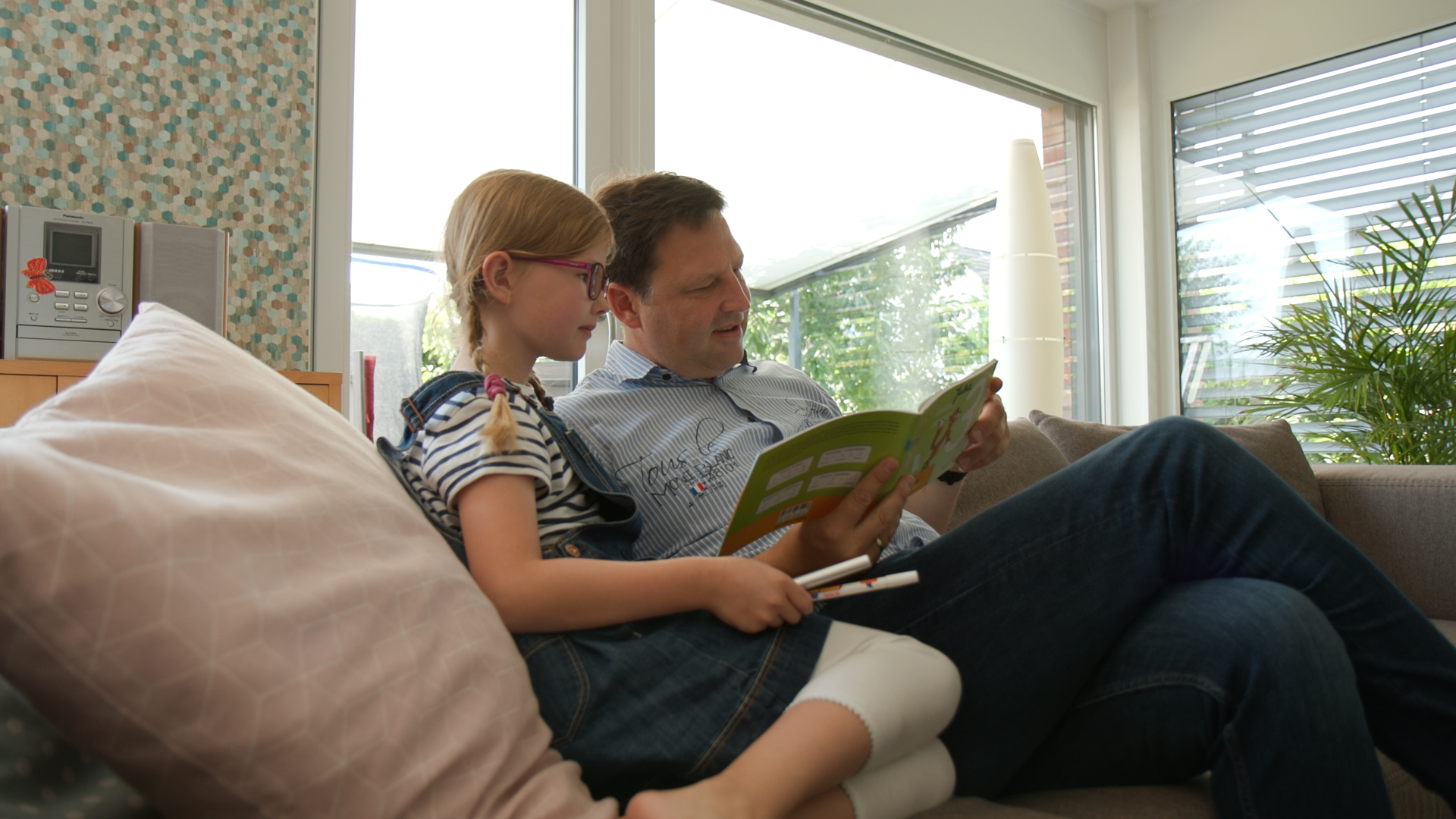 Julia und ihr Vater sitzen auf dem Sofa. Ihr Vater hält ein Buch in der Hannd. Copyright: MHH