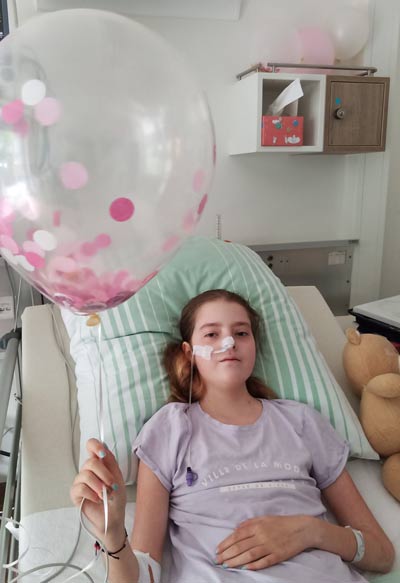 Lara im Patientenbett mit einem großen Luftballon in der Hand. Copyright: privat