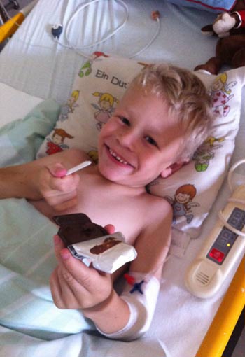 Moses liegt in seinem Patientenbett, lacht und isst Brotsticks mit Nutella. Copyright: Katharina Lücke