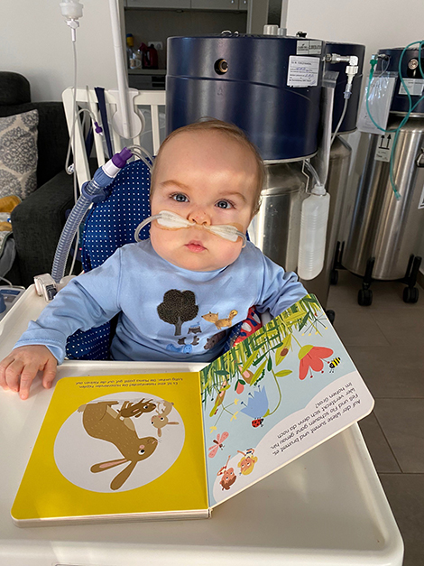 Theo sitz am Tisch und ließt ein Buch. Im Hintergrund sieht man die Sauerstoff-Container. Copyright: privat / Theos Familie