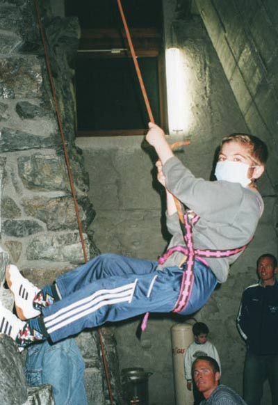 Jan hängt in einem Sicherheitsgurt an der Kletterwand. Er trägt einen Mundschutz. Copyright: privat