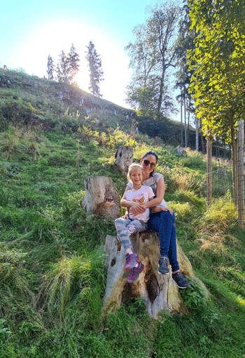 Tamara mit ihrer Tochter auf einem Baumstumpf im Grünen. / Copyright: Tamara Maier 