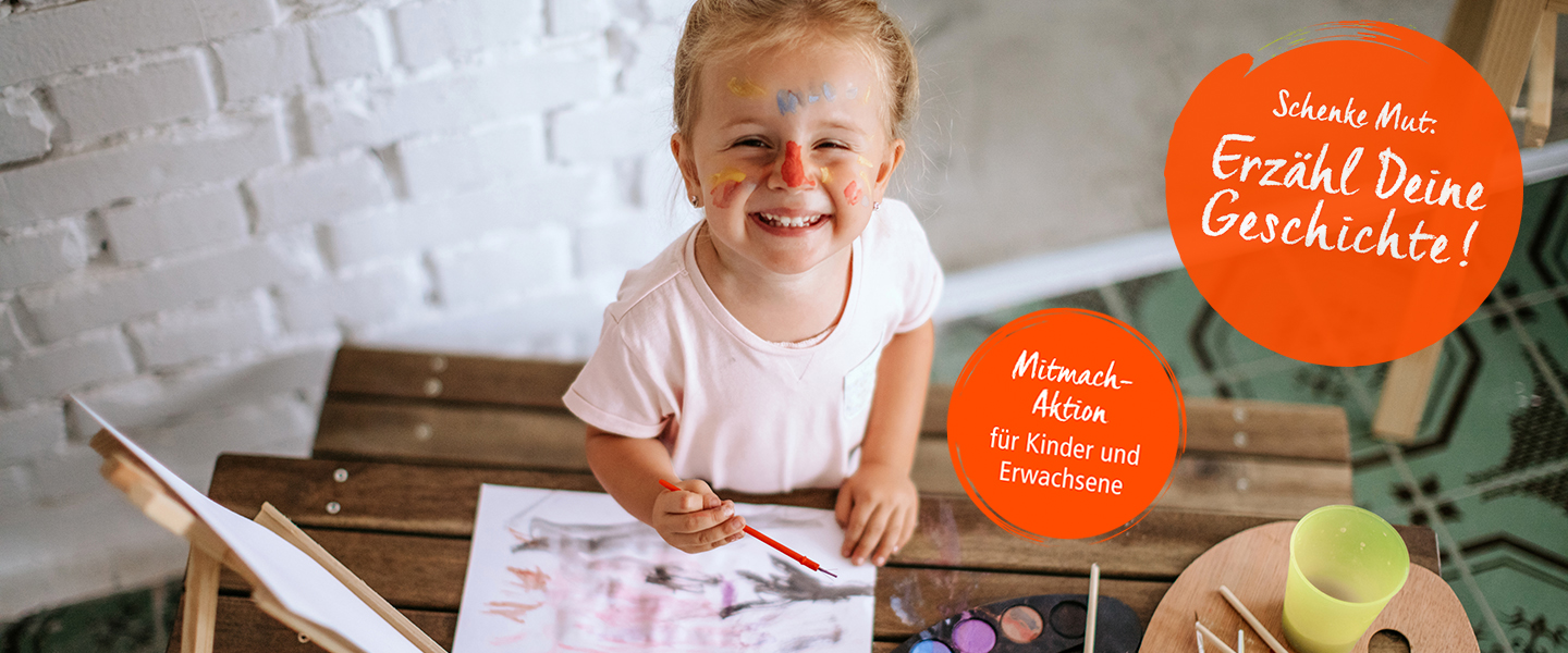 Ein junges Mädchen mit roten Tupfer auf der Nase und Pinsel in der Hand malt an einem Tisch und freut sich dabei. Ein roter Button wirbt für die Mitmach-Aktion für Kinder und Erwachsene; Copyright: iStock/StefaNikolic