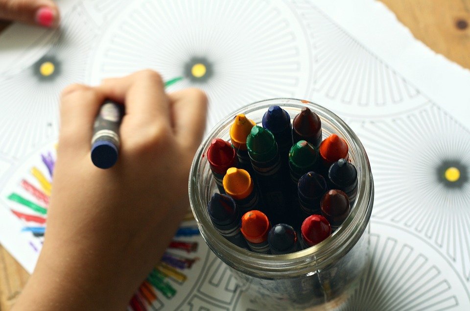 Ein Glas mit Stiften. Daneben eine Kinderhand, die mit einem Stift ein Bild ausmalt.