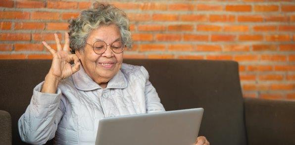 Eine ältere Dame sitzt begeistert an einem Laptop.