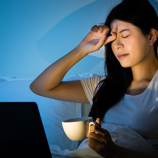 Eine Frau sitzt müde, mit Tasse in der Hand vor dem Laptop.