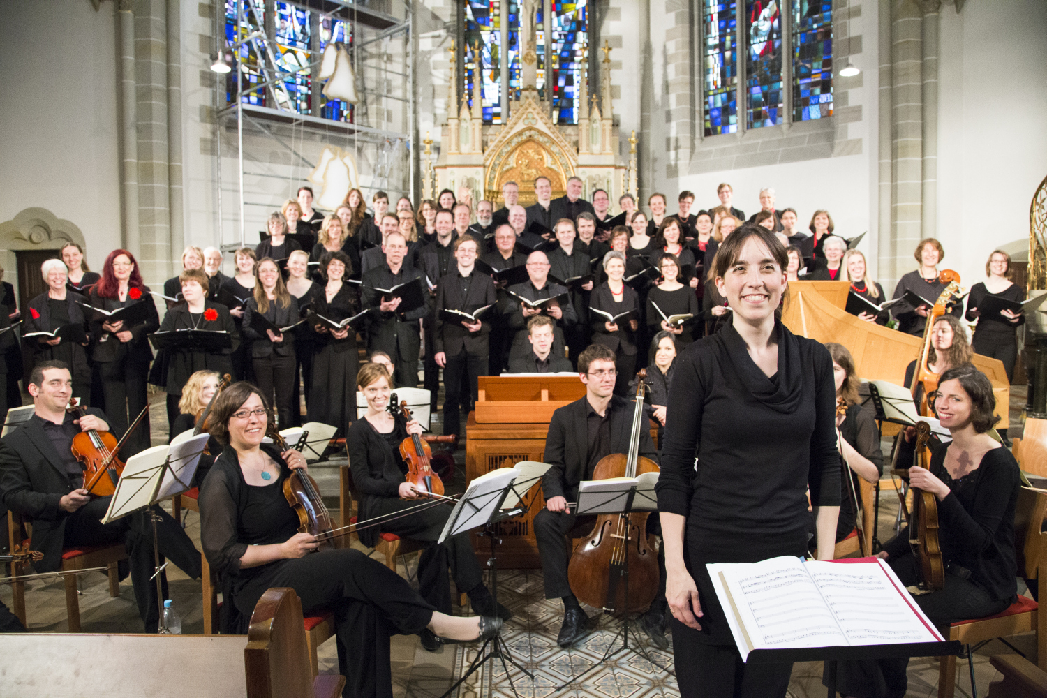 Der Chor und das Orchester bei einer Probe in der Markuskirche. Alle lächeln in die Kamera.