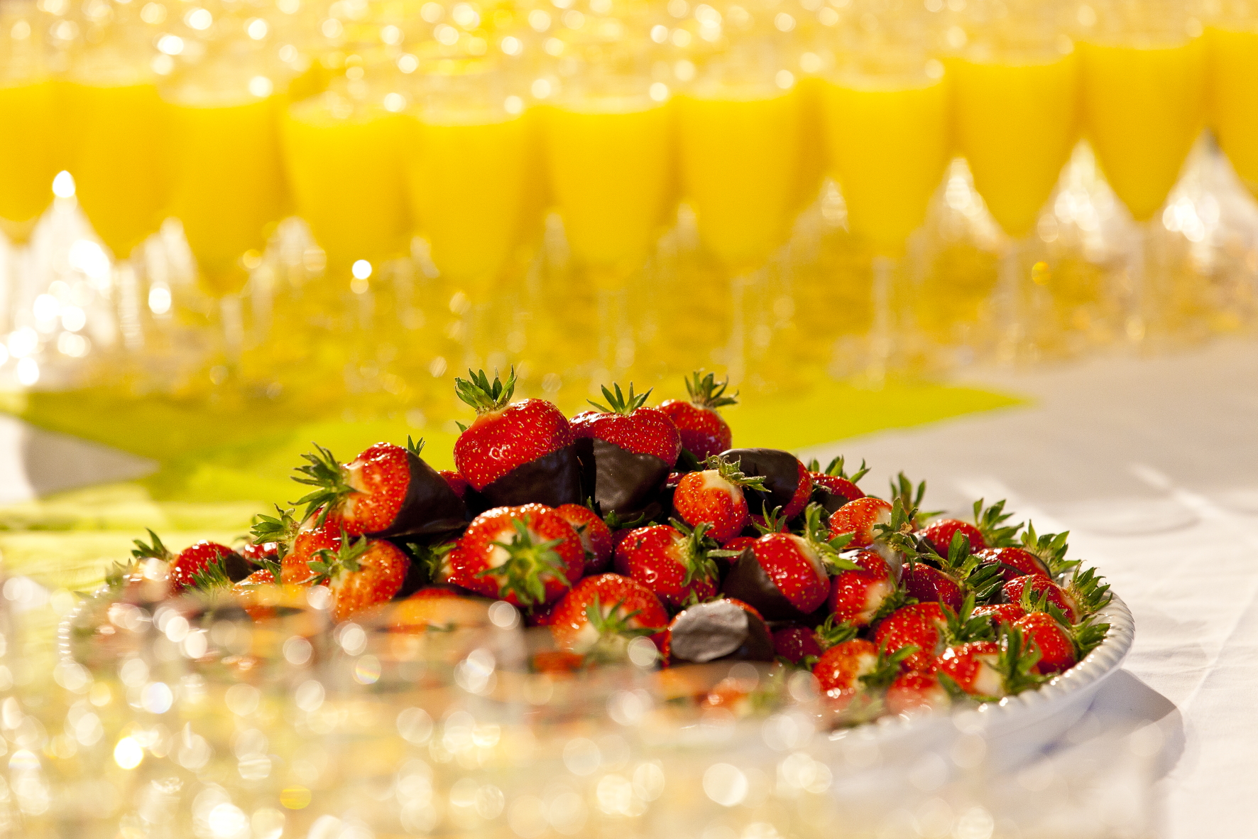 Ein Teller mit Schokoerdbeeren und im Hintergrund sind Gläser mit Orangensaft